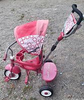 Side view of pink Radio Flyer toddler tricycle showing push handle, canopy, cup holder, footrests