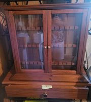 Front view of wooden spoon rack cabinet with two glass doors and lower drawer section visible