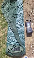 Full view of green air mattress partially unfolded beside black LED lantern on ground