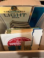 Box with visible Schlitz Light Beer sign and stacked marketing pieces