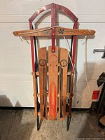 Full view of sled front showing wood slats, red arch, handlebar, rope, steel runners