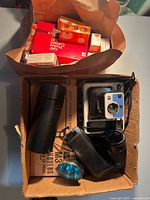 Overview of box with Kodak camera, Polaroid camera, Vivitar lens and case, flashbulbs