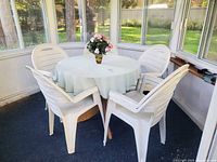 overall view of round glass table with four white resin armchairs