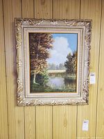 Framed oil landscape hanging on wood panel wall