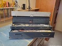 Chest open showing three drawers filled with tools and hardware