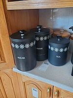Three black metal snowflake canisters