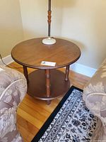 Round wooden side table between two chairs showing overall shape and two tiers