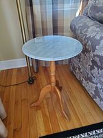 Front view of table next to sofa showing marble top and wooden tripod base