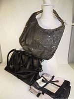 Scarf folded in foreground, black handbag and silver mesh bag displayed on mannequin
