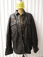 Front view of black leather Harley-Davidson shirt-jacket showing snap closure, chest pockets, logo patch