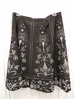 Front view of black A-line skirt displaying white/silver floral and paisley print