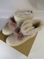 Top view of both boots on box showing suede, shearling lining and pom-poms