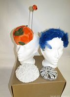 All four fascinators displayed on two mannequin heads and box