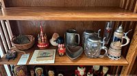 Shelf view showing two lidded steins, pewter tankard, heart dish, wicker basket and figurines