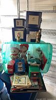 Stacked blue boxes of Greenwich Workshop ornaments, plush figures, books and other decor in bin