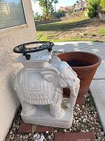 Elephant plant stand with trivet on top beside large terracotta planter pot