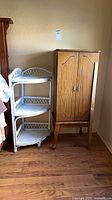 Jewelry armoire next to wicker corner shelf showing full view of both items