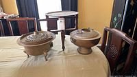 Two brass cookware pieces and wooden folding table displayed on dining table