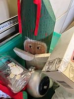 Green tote filled with assorted Christmas items including wooden Santa, glass snowman tumbler and ornament boxes