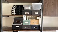 Group of storage containers on shelf: plastic magazine holder, plastic bins, drawer boxes, lidded photo boxes