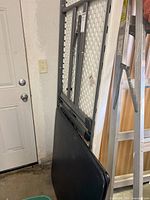 Folded plastic banquet table and edge of card table leaning against wall