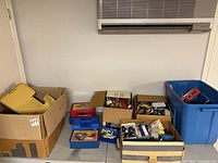 Overview of cardboard boxes, blue tote and plastic carry cases containing die-cast vehicles