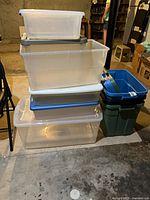 Stack of seven assorted plastic totes showing colours, lids, and condition