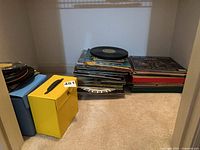 Stack of vinyl records alongside blue and yellow carrying cases