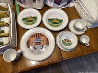 Plates, bowls, cups and saucers on table showing various Design Naïf scenes