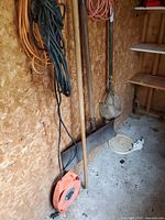 Group of tools and cords in shed, showing shovel, tamper, blade, cords and reel