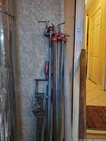 Group of six long pipe bar clamps leaning against wall
