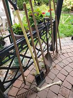 Group shot of all long-handled garden tools leaning against patio railing