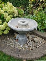 Full view of gray cast stone bird bath fountain in garden setting