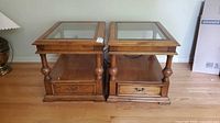 Front view of both oak end tables showing glass tops, drawers, shelves, turned legs