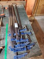 Six long bar clamps laid on workbench, full view