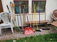 Full view of assorted shovels, brooms, rake, cultivator and tiki torches leaning against wall
