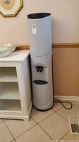 Full view of cylindrical gray water cooler next to cabinet