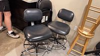 Two black vinyl rolling office chairs beside folded metal chairs
