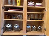 Cabinet shelves showing glass storage jars, glasses, bowls and additional items