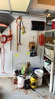 Pegboard with rakes, hedge trimmer, bow saw, snow shovel, extension cord, sprayers and bags below