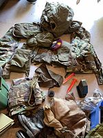 Assorted military clothing, parka, boots, belts, stakes, ammo can laid out on floor