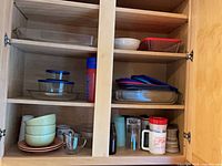 Cabinet shelves showing Pyrex bakeware, storage bowls with lids, assorted drinkware and ceramics