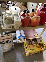 Shelf cart showing 3 gas cans, hamper of items, joint compound bag, box of tiles and misc