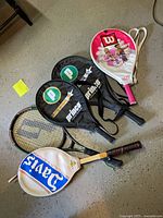 Five rackets arranged on floor showing covers and uncovered racket