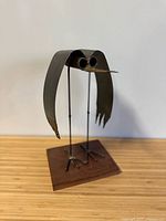 Front view of signed brutalist metal bird sculpture on wood base