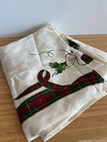 Folded ivory Lenox Christmas tablecloth showing plaid ribbon and holly design