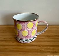 Side view of Mackenzie-Childs enamel mug showing pink background with yellow polka dots and checkerboard band