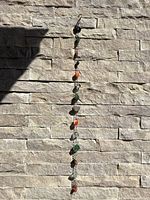 Full view of entire rain chain hanging against stone wall