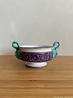 Front view of footed ceramic bowl showing blue band with gold scrolls and turquoise handles