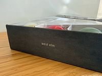 West Elm branded grey box with clear lid showing multiple ornaments